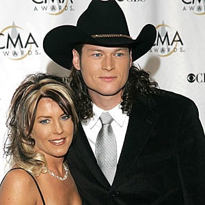 Blake Shelton in a black hat, white shirt and black coat posing with Kaynette Williams in a black dress.